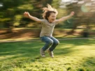 Criança sorridente pulando alegremente em um parque verde, ilustrando a importância do movimento para o aprendizado infantil.