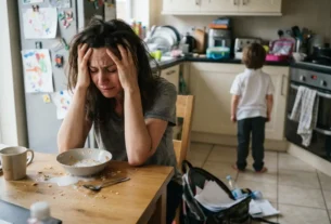 Mãe exausta com as mãos na cabeça demonstrando estresse e falta de paciência com os filhos de manhã.